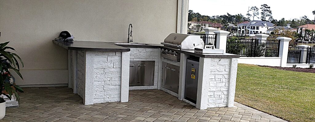 Grande Dunes custom outdoor kitchen in Myrtle Beach featuring counter-height seating, full-sized granite composite sink, commercial 304 stainless steel grill, refrigerator, and ample storage with stunning Intracoastal Waterway views
