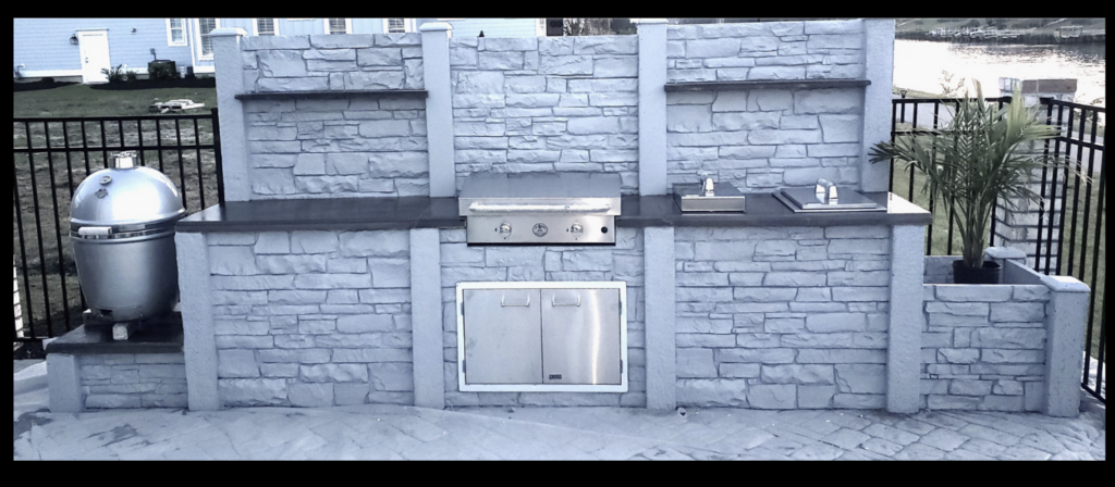 Custom luxury outdoor kitchen in Del Webb Grande Dunes Myrtle Beach with precast concrete cabinetry, flat top griddle, Kamado grill, and privacy backsplash with built-in shelving