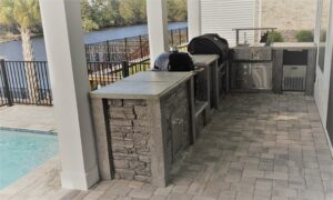 StoneKitchen outdoor kitchen with grill and Kamado cooker beside a pool and waterway in North Myrtle Beach