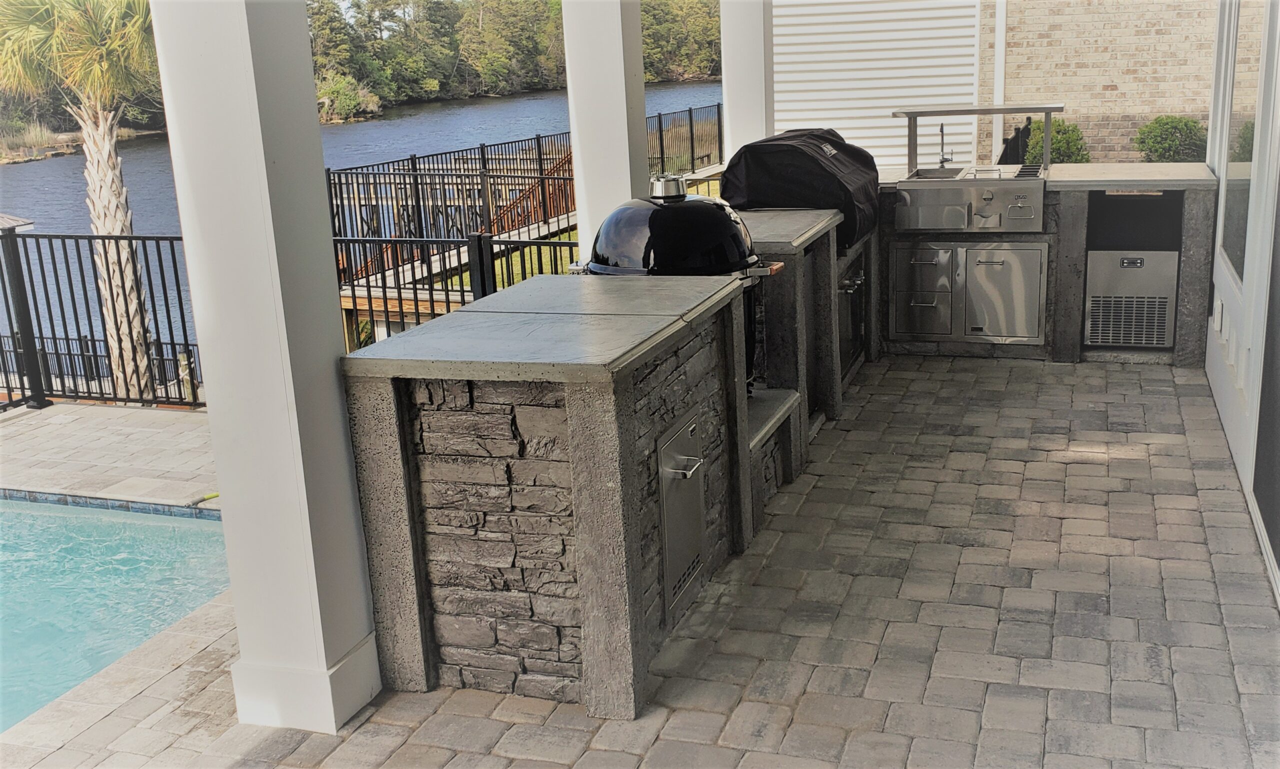 StoneKitchen® outdoor kitchen with grill and Kamado cooker beside a pool and waterway in North Myrtle Beach